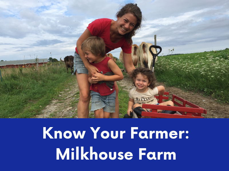 A smiling woman and two young children are on a dirt path in a grassy field with cows in the background.