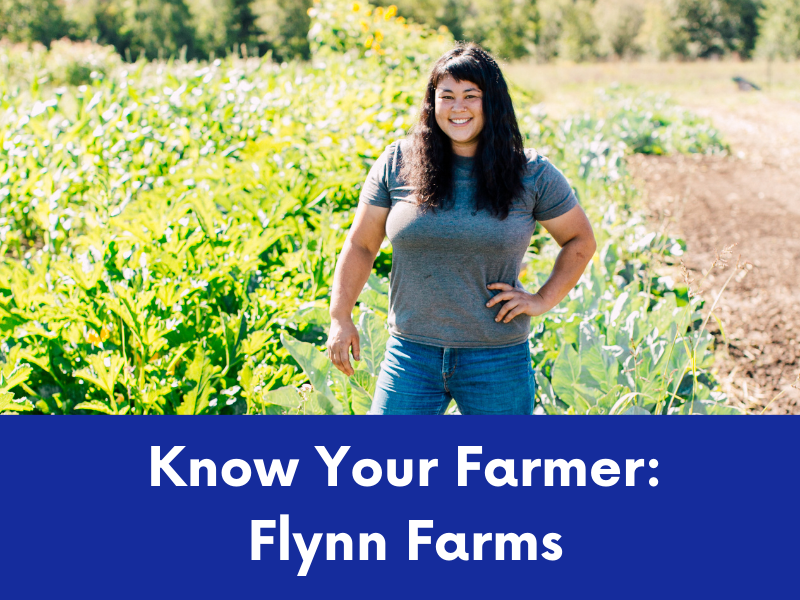 A smiling farmer with dark hair stands in a lush green field with her hand on her hip.