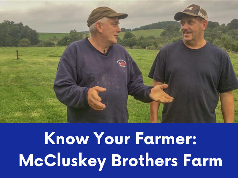 Two men, likely the McCluskey brothers, wearing caps and casual clothing, are talking in a green field.