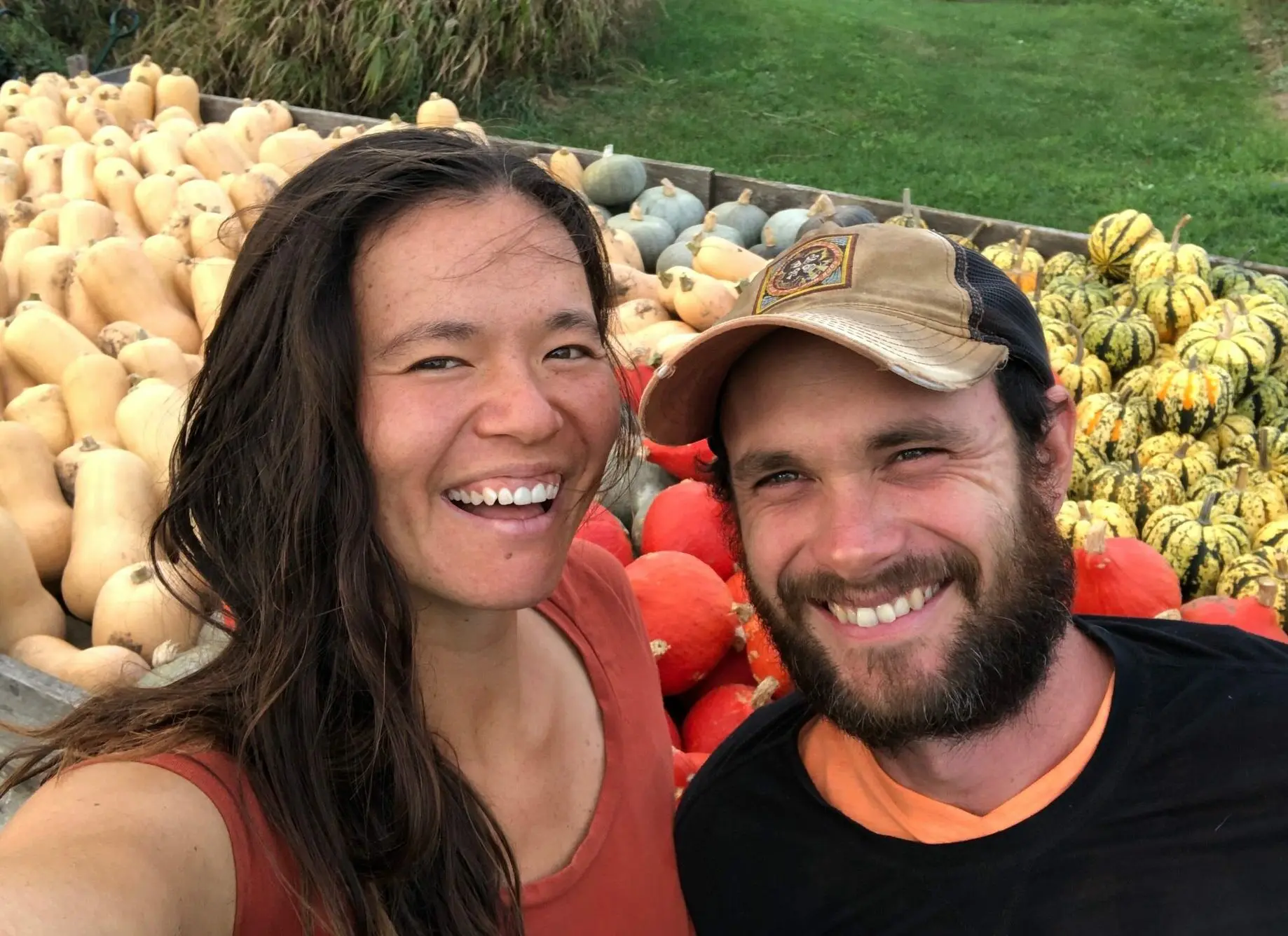 Farmers standing in front of a colorful harvest of organic squash and pumpkins.