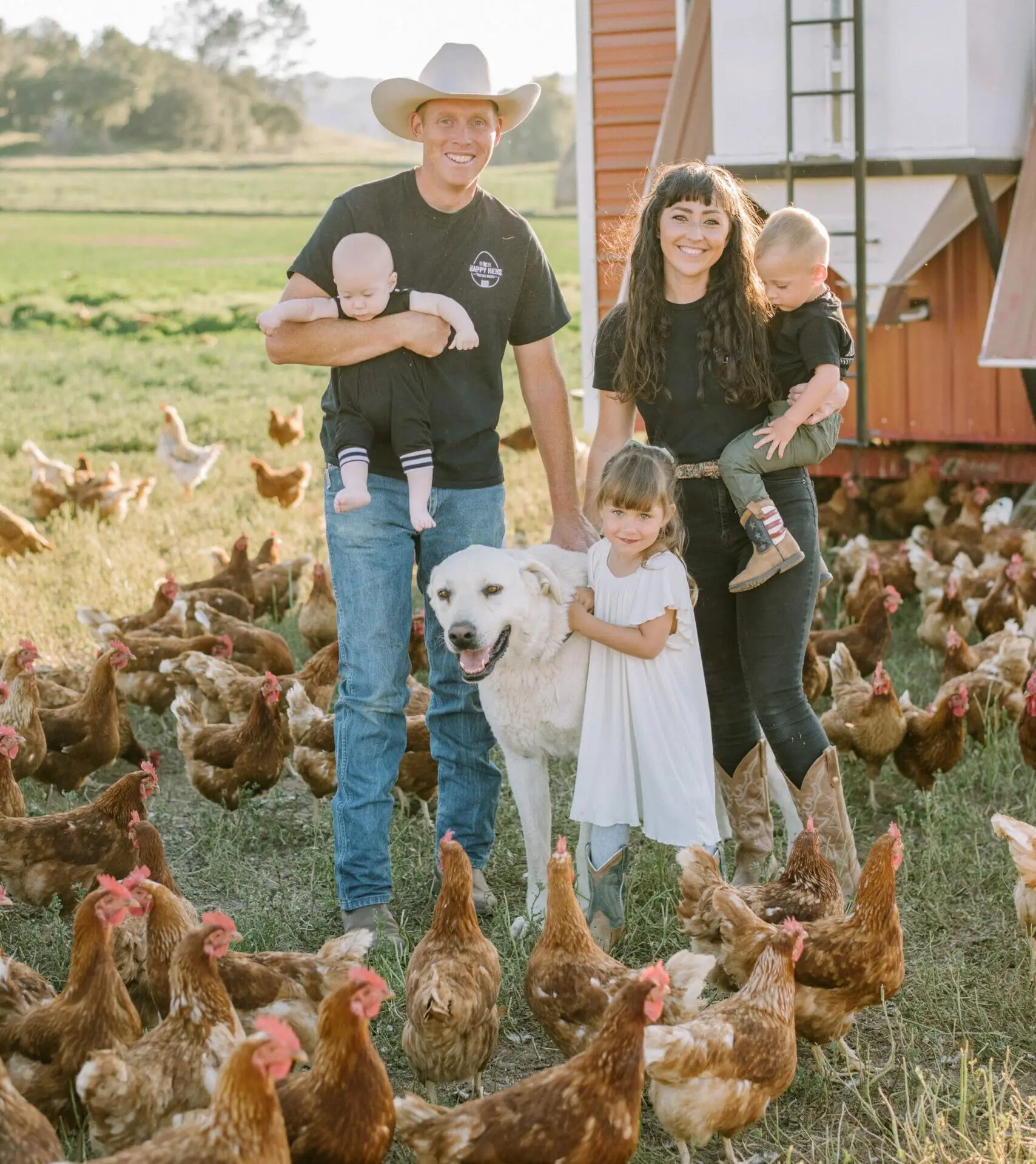 Family standing in a pasture surrounded by pasture-raised chickens on an organic farm.