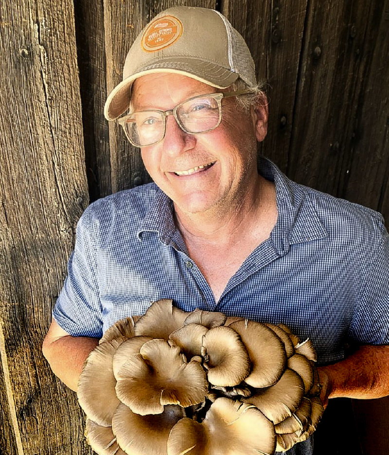 Alan Lewis holds a gigantic edible mushroom and smiles in a tan baseball cap