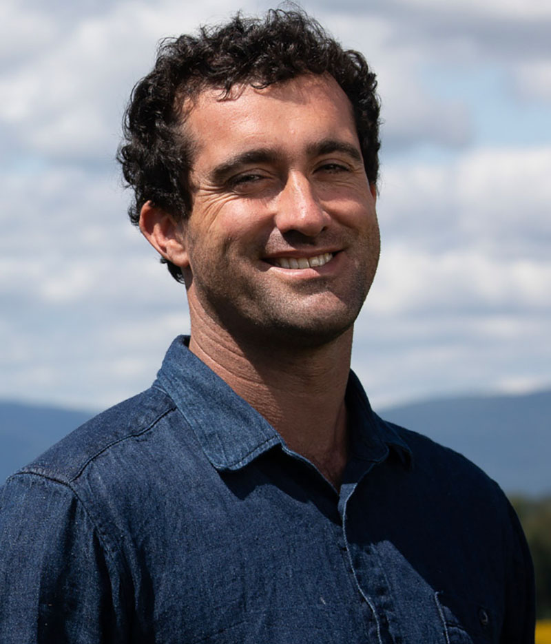 Ben Dobson smiling in a grain field wearing a denim shirt