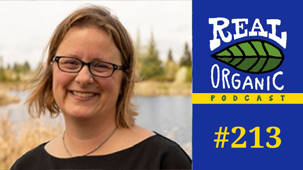 soil scientist Jennifer Pett-Ridge smiles in a black shirt, glasses, and necklace with a marsh behind her