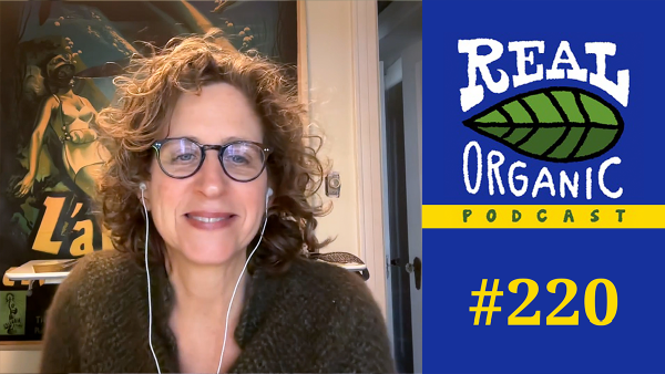 Environmental journalist Sharon Lerner smiles from her desk wearing earpbuds for her interview about PFAs in our food with Dave Chapman