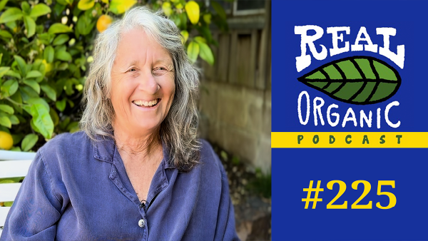 Julie Guthman smiles in a blue button down shirt in her California yard