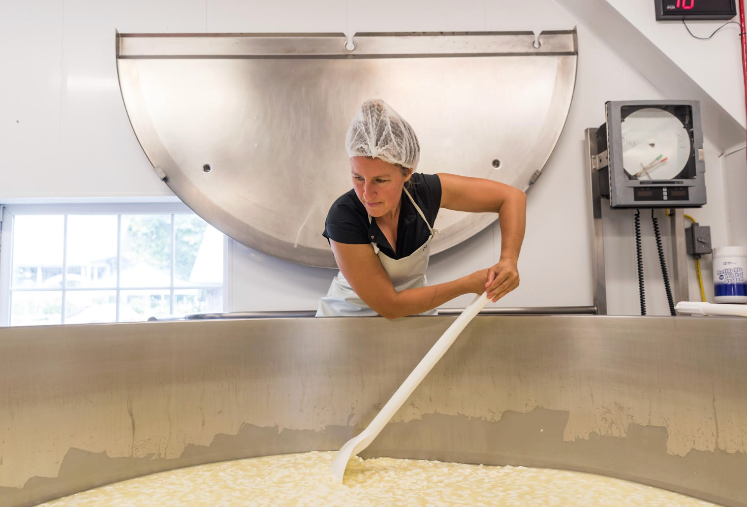 Molly Semler stirs a vat of dairy with a paddle.