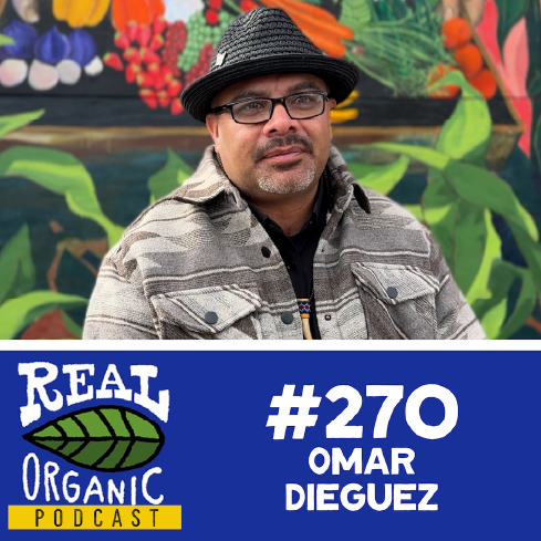 Omar Dieguez in a black hat and glasses seated in front of a colorful mural