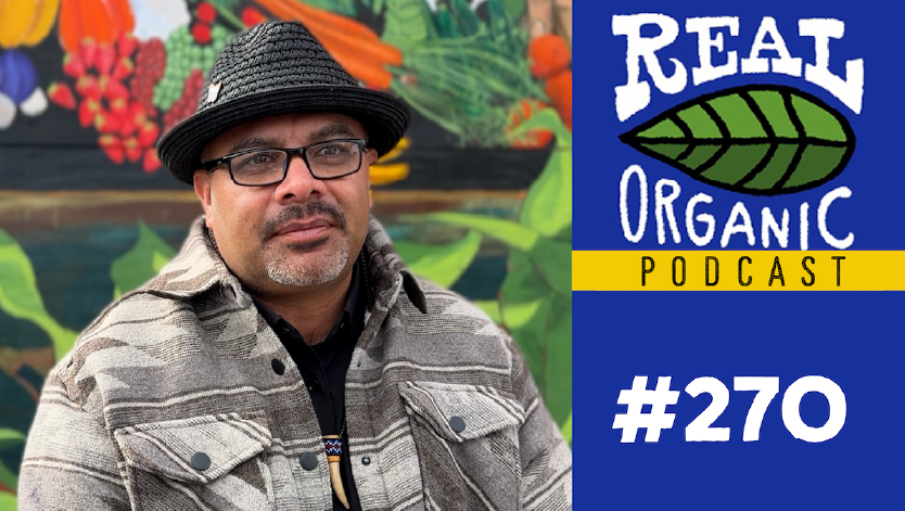 Omar Dieguez in a black hat and glasses seated in front of a colorful mural